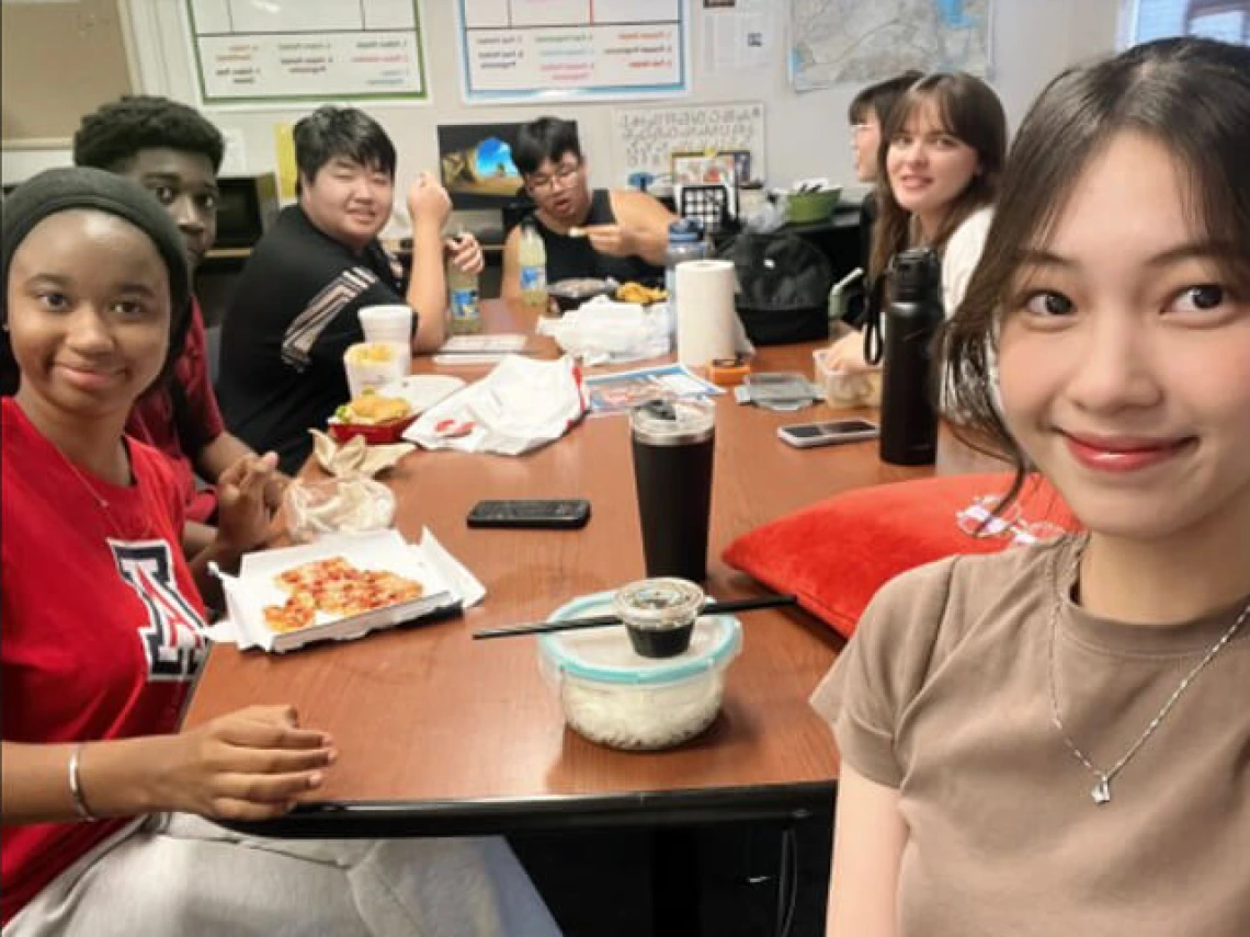 Students gathered around classroom table for pizza lunch